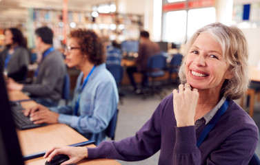 Portrait Of Female Mature Adult Student In Class Working At Computers In College Library