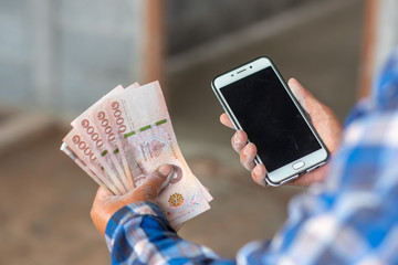 The hands of the construction workers holding banknotes and mobile phones