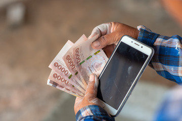 The hands of the construction workers holding banknotes and mobile phones