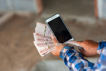 The hands of the construction workers holding banknotes and mobile phones