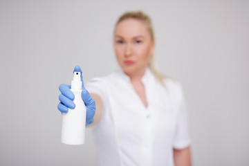 health care, hygiene and corona virus pandemic concept - female doctor, nurse or cosmetologist in white uniform spraying disinfective liquid over gray