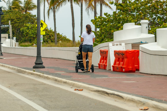 Mother texting on her cell phone white walking down the Fort Lauderdale Beach boardwalk while pushing a baby stroller. 