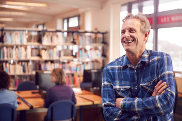 Obraz premium Portrait Of Mature Male Teacher Or Student In Library With Other Students Studying In Background