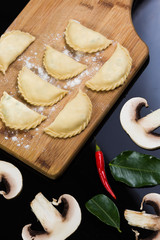 Semi-finished dumplings on a wooden board on black background