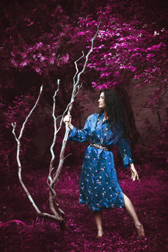 young woman in blue kimono stand in infrared garden holding big white branch