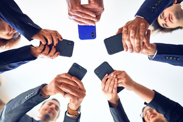 Group of business workers smiling happy and confident. Standing on a circle with smile on face using smartphone together at the office.