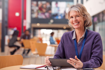 Portrait Of Mature Female Teacher Or Student With Digital Tablet Working At Table In College Hall