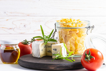 Ingredients for cooking close up. Raw Italian farfalle pasta, blue cheese, ripe tomatoes and spices on white wooden background. Healthy food concept.