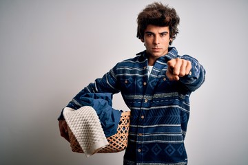 Young handsome man holding wicker basket with clothes over isolated white background pointing with finger to the camera and to you, hand sign, positive and confident gesture from the front