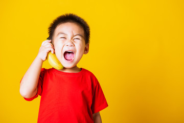 child or kid cute little boy attractive smile playing holds banana fruit pretending to be like a telephone
