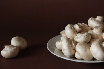raw mushrooms on a plate on dark brown background