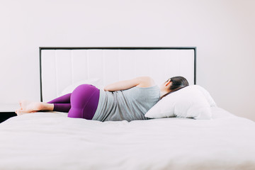 Young woman doing exercises at home while quarantine, do sports while self-isolation, home yoga, woman in purple leggins on the bed.