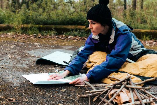 Concentrated young female backpacker searching location on map while sitting on ground during trekking in forest in autumn day
