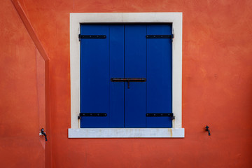 Window with closed blue shutters on an orange wall
