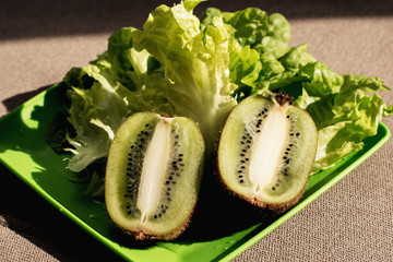 Two half juicy ripe kiwi fruit, fresh lettuce on plastic plate. Green background. Salad leaf....
