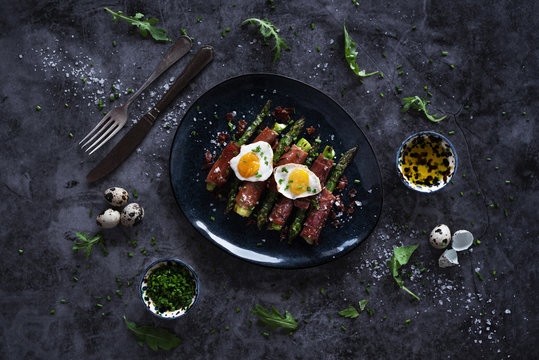 From above tasty asparagus with fried quail eggs and herbs placed on bowl near silverware on marble tabletop