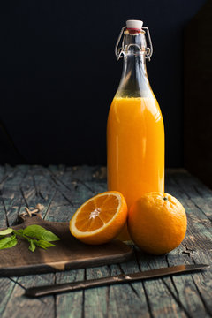 Bottle of fresh citric orange juice placed near halves of fresh oranges on a wooden dark rustic table at dark background