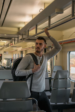 Concentrated young man with backpack holding handrail while standing in empty subway car