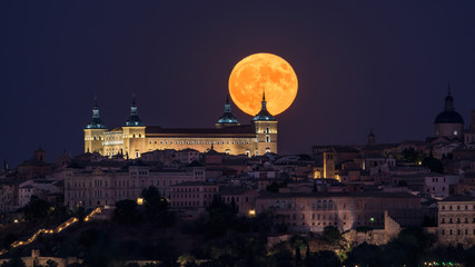 Wonderful scenery of illuminated ancient palace built over town in colorful night with full red Moon in Toledo