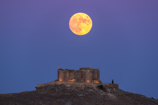 From below picturesque scenery of abandoned aged fortress on top of mountain illuminated by full Moon at night in Toledo