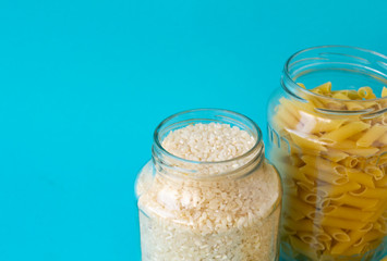 Noodles, rice, pasta in glass jars stand on a blue background. Raw materials for cooking.