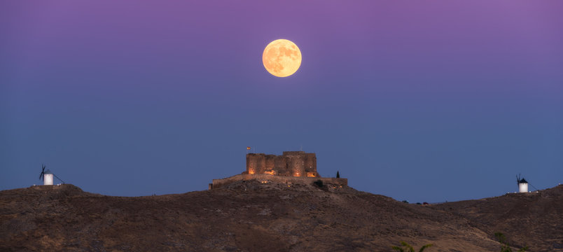 From below picturesque scenery of abandoned aged fortress on top of mountain illuminated by full Moon at night in Toledo