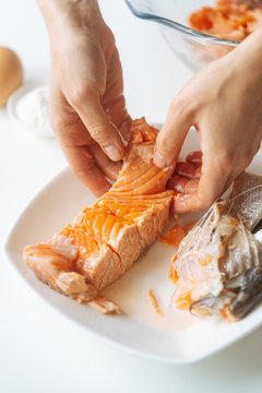 Crop hands of female separating piece of cooked salmon from bones while preparing dinner at home