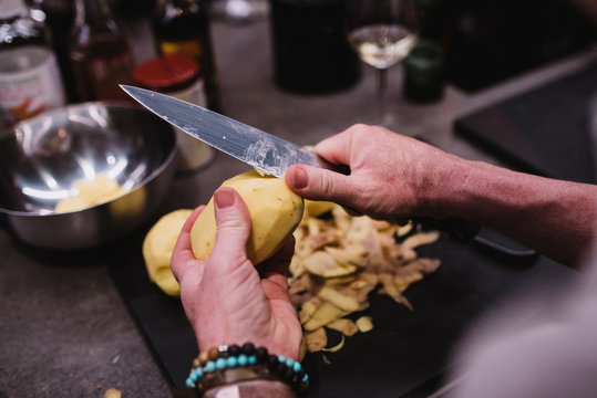 From above anonymous person with bracelet using sharp knife to peel fresh potato over in kitchen during cooking lesson in Navarre, Spain