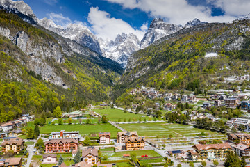 The Improbable aerial landscape of village Molveno, Italy, snow covered mountains Dolomites on background, roof tops of chalet, sunny weather
