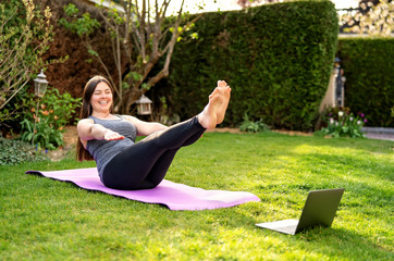 Happy smiling woman practicing pilates lesson online in garden outdoors during quarantine. Doing...