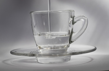 Close-up of water pouring into a small glass beaker, on a white background