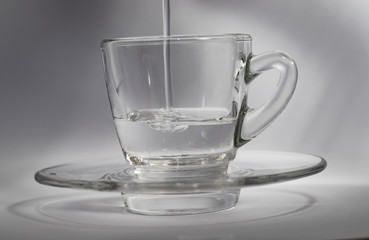 Close-up of water pouring into a small glass beaker, on a white background