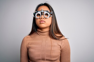 Young asian optical girl controlling eyesight using optometry glasses over white background with serious expression on face. Simple and natural looking at the camera.