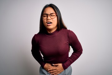 Fototapeta premium Beautiful asian business woman wearing casual sweater and glasses over white background with hand on stomach because nausea, painful disease feeling unwell. Ache concept.