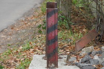 one striped iron fence post from an old rail stands on the street by the road