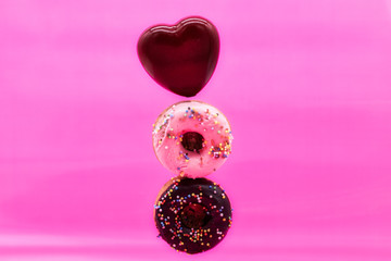 Various decorated doughnuts and red heart in motion falling on pink background. Sweet and colourful doughnuts falling or flying in motion.