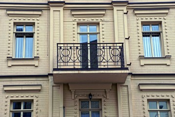 one open black iron balcony with a wrought pattern on a brown brick wall with windows and a glass door on the street