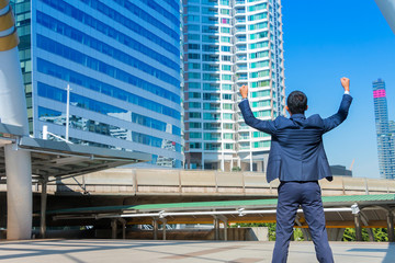 Successful businessman celebrating his victory with arms up with cityscape background.