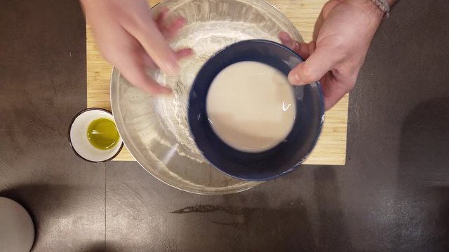 man adds the fresh brewer's yeast dissolved in lukewarm water to some flour in a bowl and then mix everything and obtain the pizza dough, in the home kitchen during the lockdown for the covid 19
