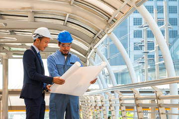 Engineer and worker with helmet looking paper plans at construct