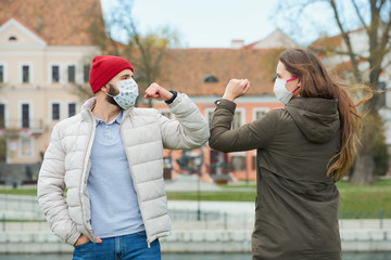 Obraz premium Elbow bumping. Elbow greeting to avoid the spread of coronavirus (COVID-19). A man with a beard and a woman with long hair in medical masks bump elbows instead of greeting with a hug or handshake. 