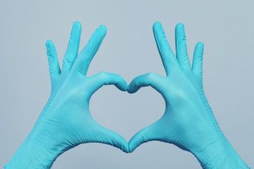 Hands in blue doctor gloves making heart on gray background. Medical assistance concept