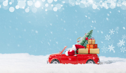 Santa Claus in Red car carrying christmas tree and presents at snowy background. Christmas background. Holidays card. Copy space.