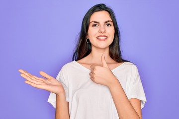Obraz premium Young beautiful brunette woman wearing casual white t-shirt over purple background Showing palm hand and doing ok gesture with thumbs up, smiling happy and cheerful