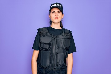 Young police woman wearing security bulletproof vest uniform over purple background winking looking at the camera with sexy expression, cheerful and happy face.