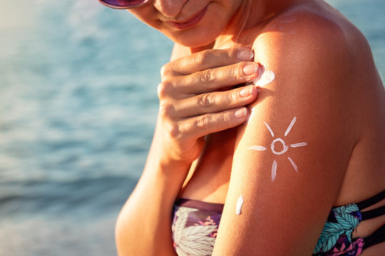 Smiling Young Woman Applying Sun Block Cream On Beach.