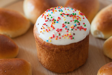 homemade easter cake with white sugar glaze and color sprinkle near patties on wooden board