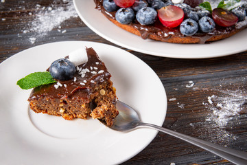 piece of chocolate cake with fresh blueberries and mint on a white saucer on a dark wooden , dessert