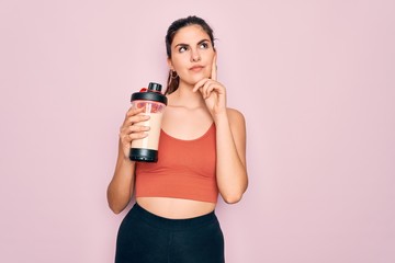 Young beautiful fitness woman wearing sport excersie clothes drinking protein shake serious face...
