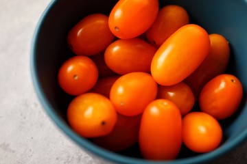 Closeup of cherry tomato in blue bowl on marble table. Macro, top view, horizontal.